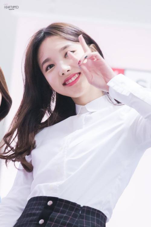 Image: Nayeon giving fans a big smile as she puts up a "V" sign / Fan take photo, credited as tagged