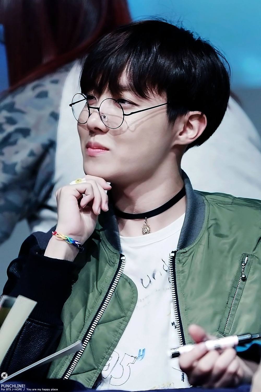 BTS' J-Hope wore his slim black choker with a army green bomber jacket an a pair of delicate circular glasses. 